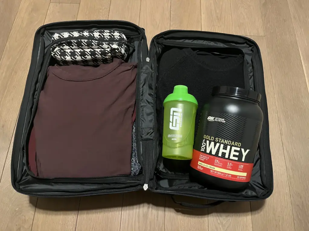 Wheyprotein und ein Shaker liegen in einem Handgepäck Koffer